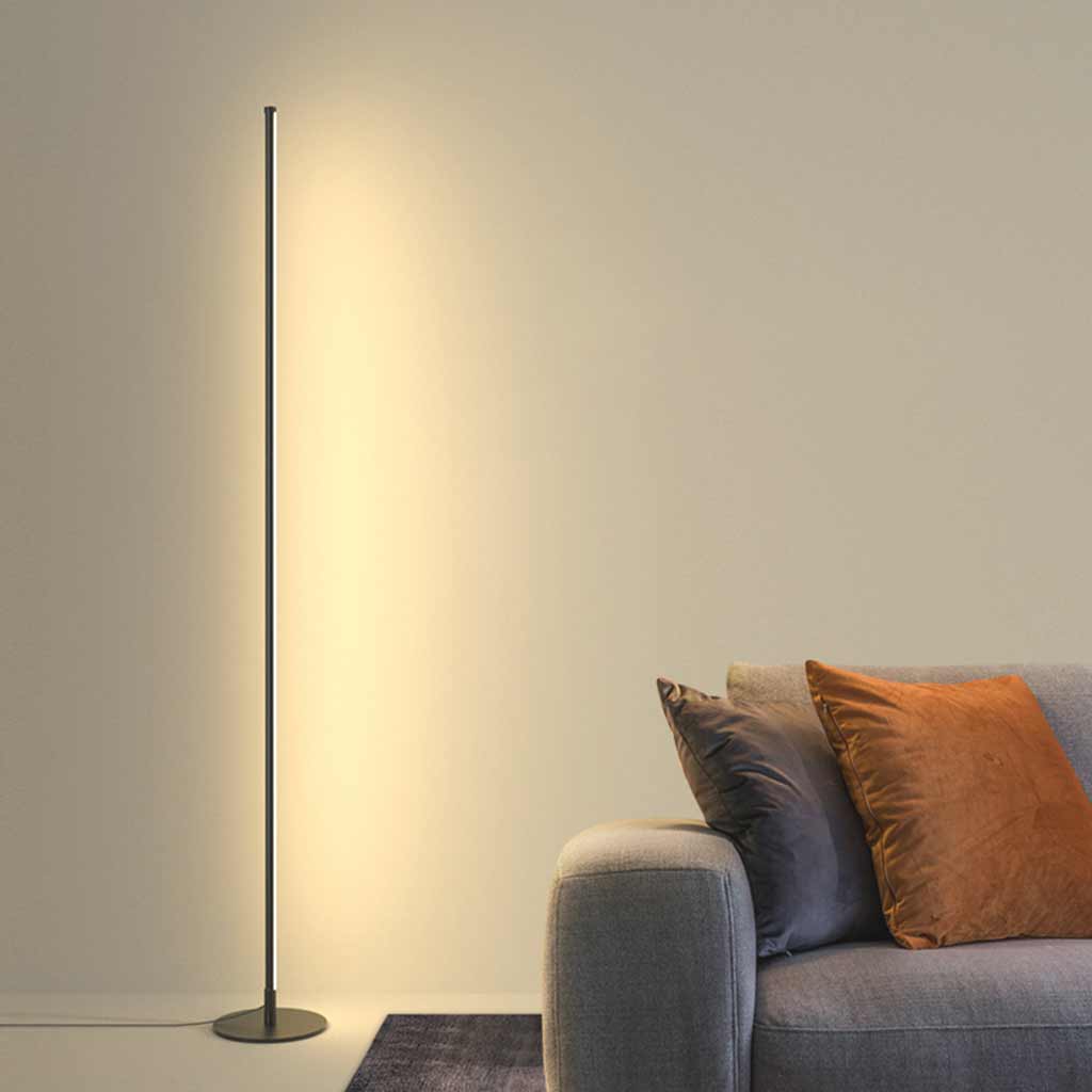 Czarna lampa stojąca LED obok szarej sofy z ciepłym światłem na ścianie