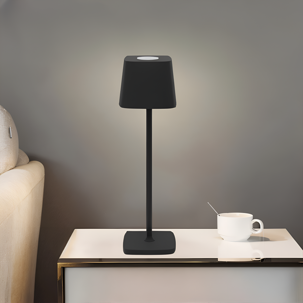 Czarna lampa bezprzewodowa świeci na komodzie obok filiżanki