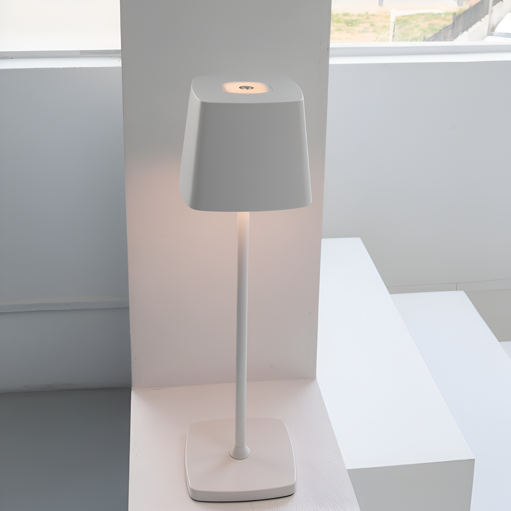 Biała lampa stołowa zapalona na białych bryłach przy oknie