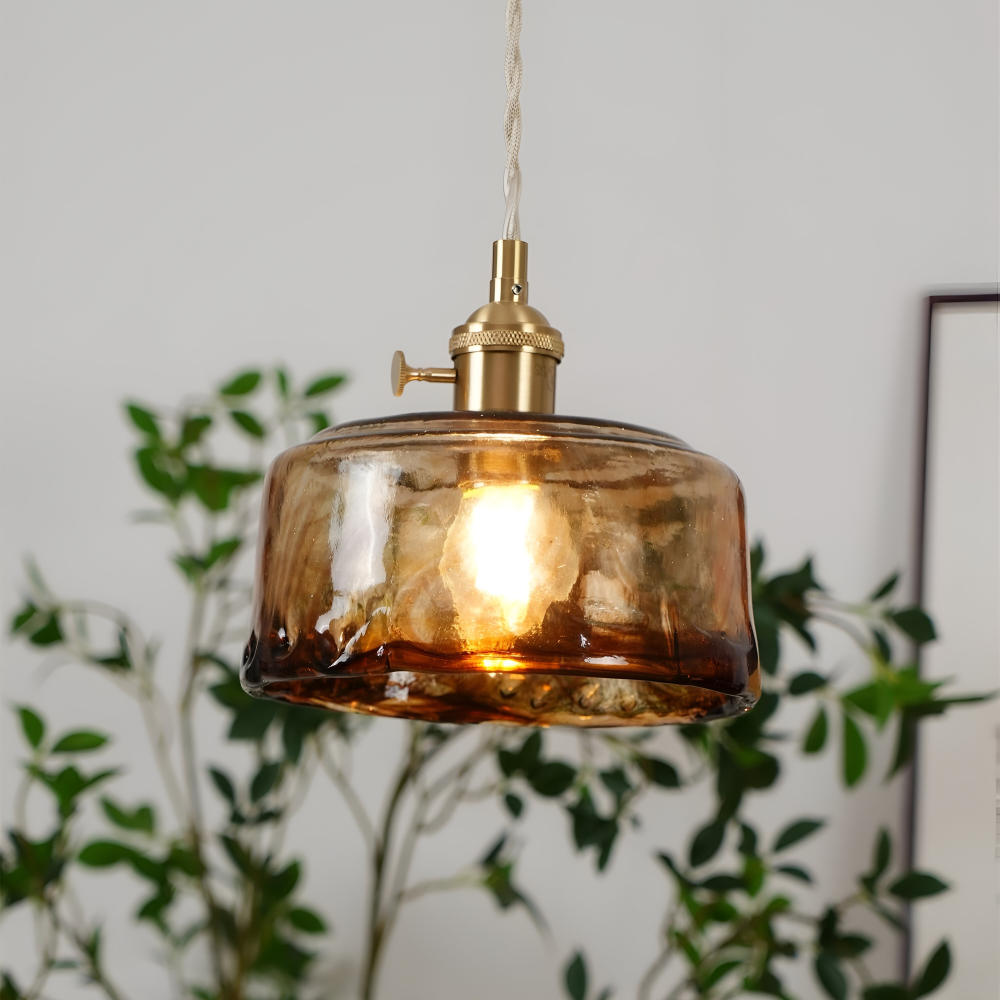 Lampa wisząca z bursztynowym kloszem na tle zielonej roślinności
