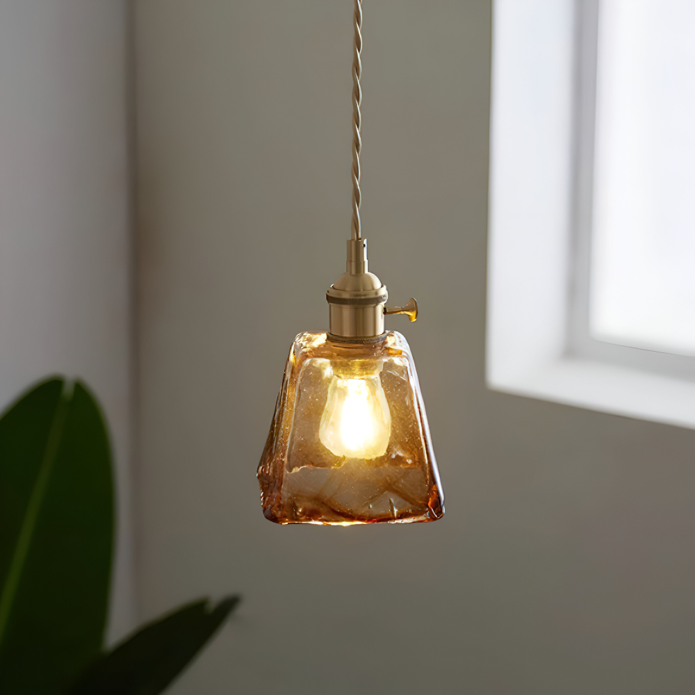 Lampa wisząca ze stożkowym kloszem przy oknie, obok tropikalna roślina