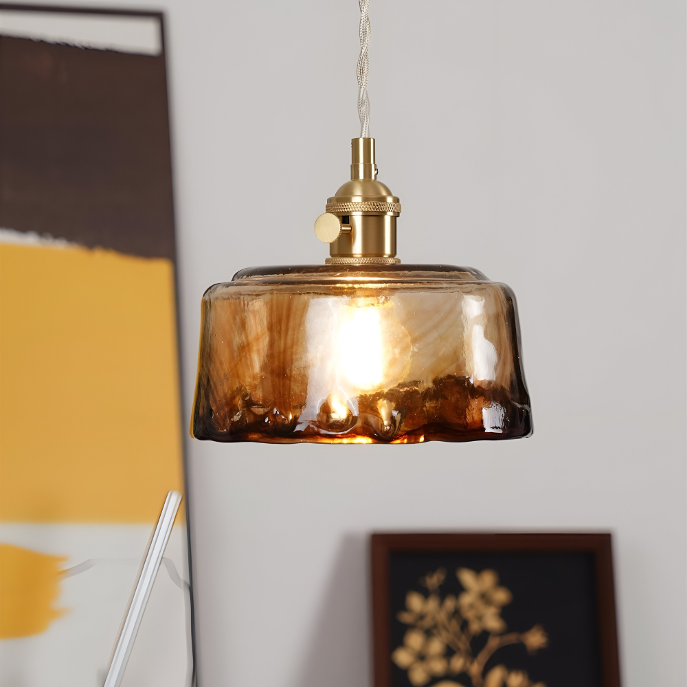 Zapalona lampa wisząca z bursztynowym kloszem na tle białej ściany
