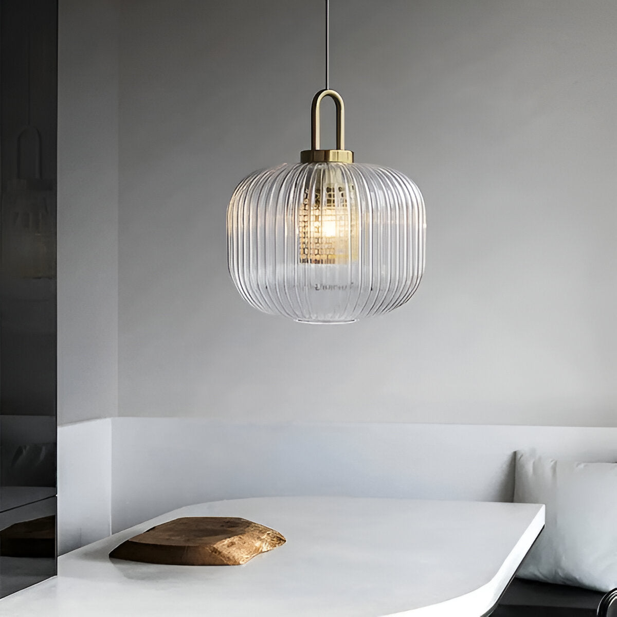 Przezroczysta żłobiona lampa wisząca nad białym stołem przy szarej ścianie