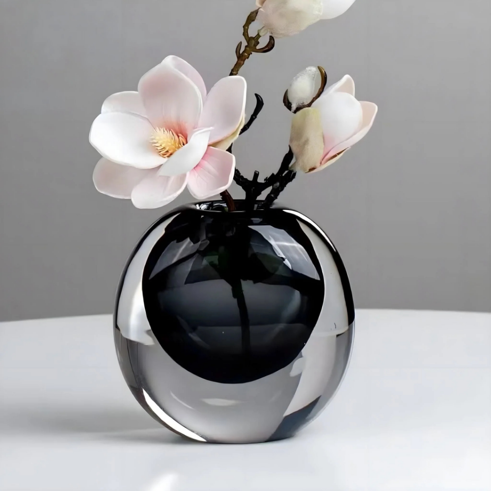 Czarny wazon szklany w kształcie kuli z gałązką magnolii na jasnym stole