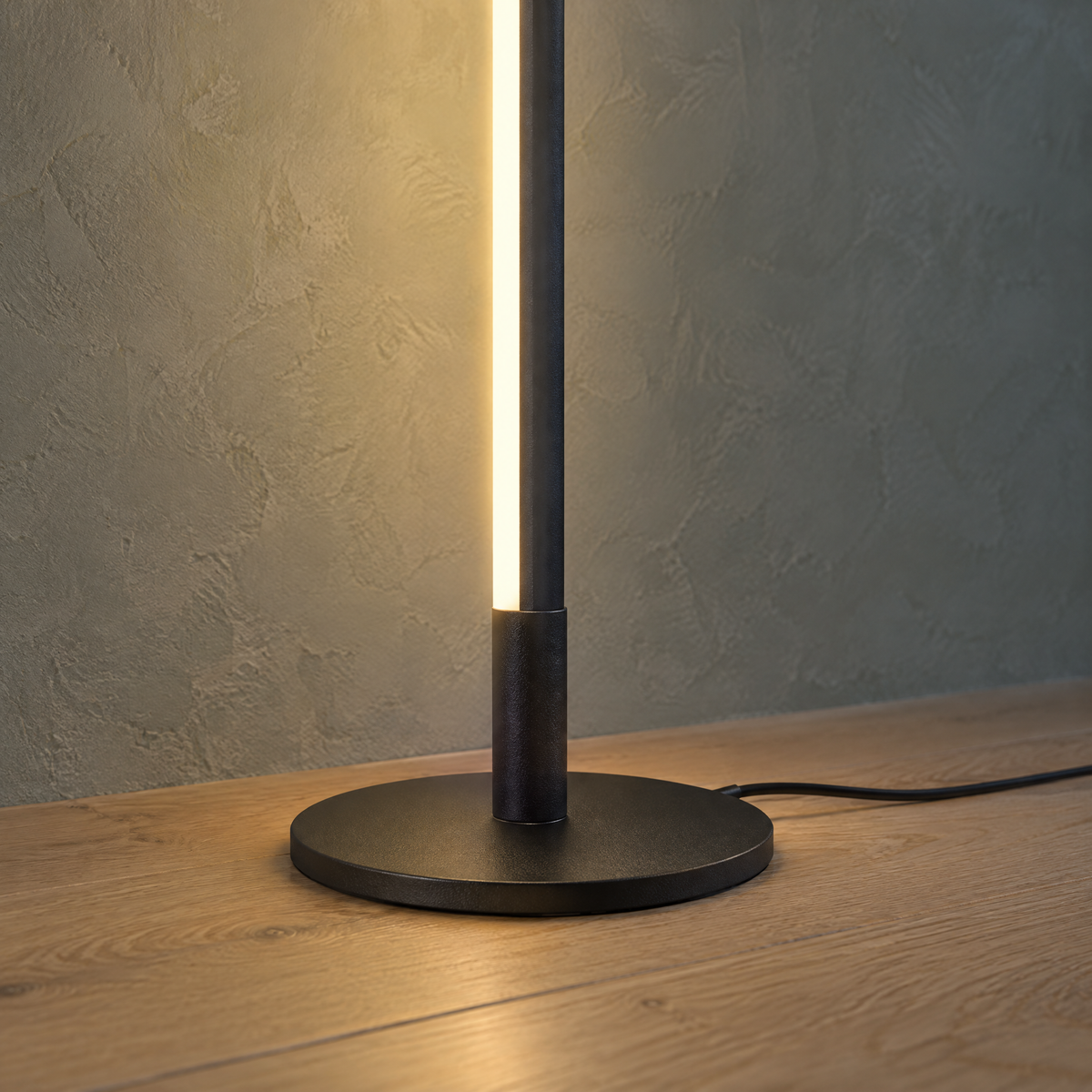 Detal lampy stojącej LED: okrągła czarna podstawa, świecąca listwa i przewód zasilający