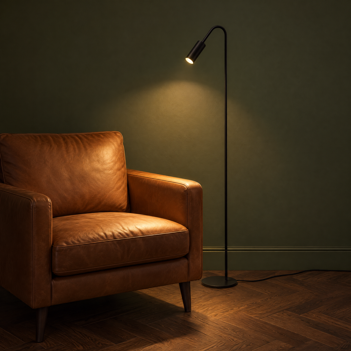 Wygięta lampa stojąca w kolorze czarnym jako lampa do czytania obok skórzanego fotela, włączona, z przewodem