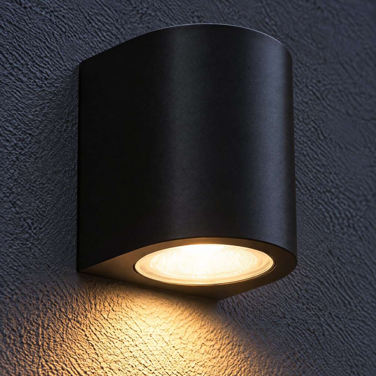 Lampa zewnętrzna LED półokrągła 3 W w kolorze czarnym na ciemnej ścianie, ciepłe światło pada z oprawy w dół